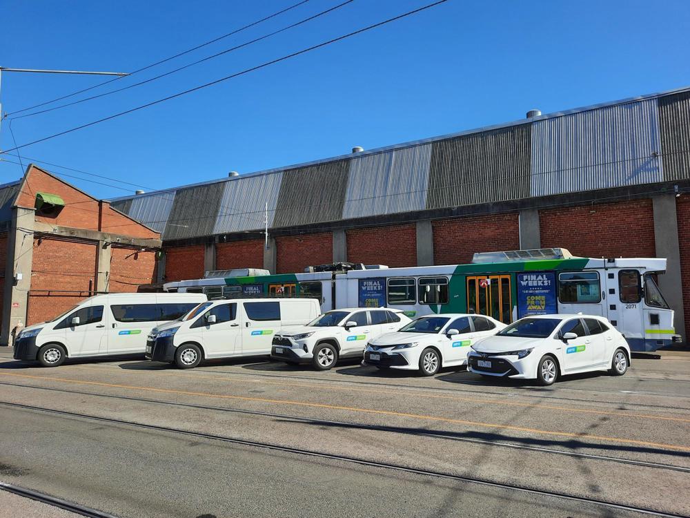 Photo: Five white vehicles parked in front of a tram at a depot